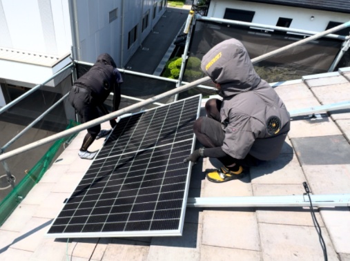 屋根の上で太陽光パネルを設置するスタッフ